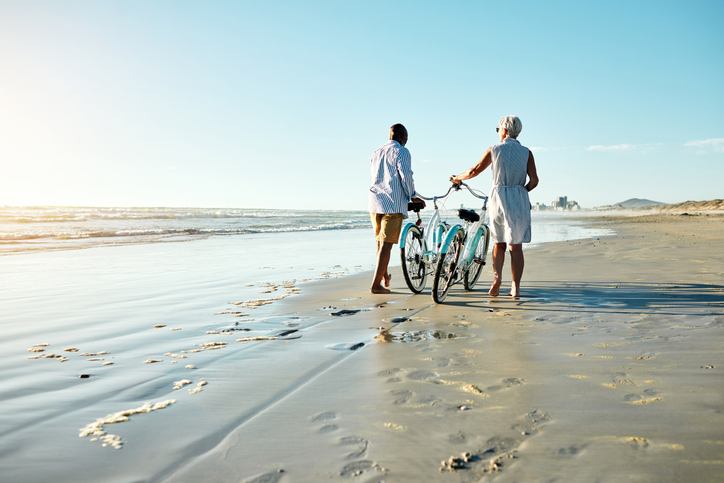 older couple walking their bikes on wide open beach